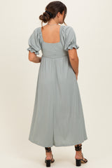 woman wearing a sage green pleated maternity dress with puff sleeves and a square back view.