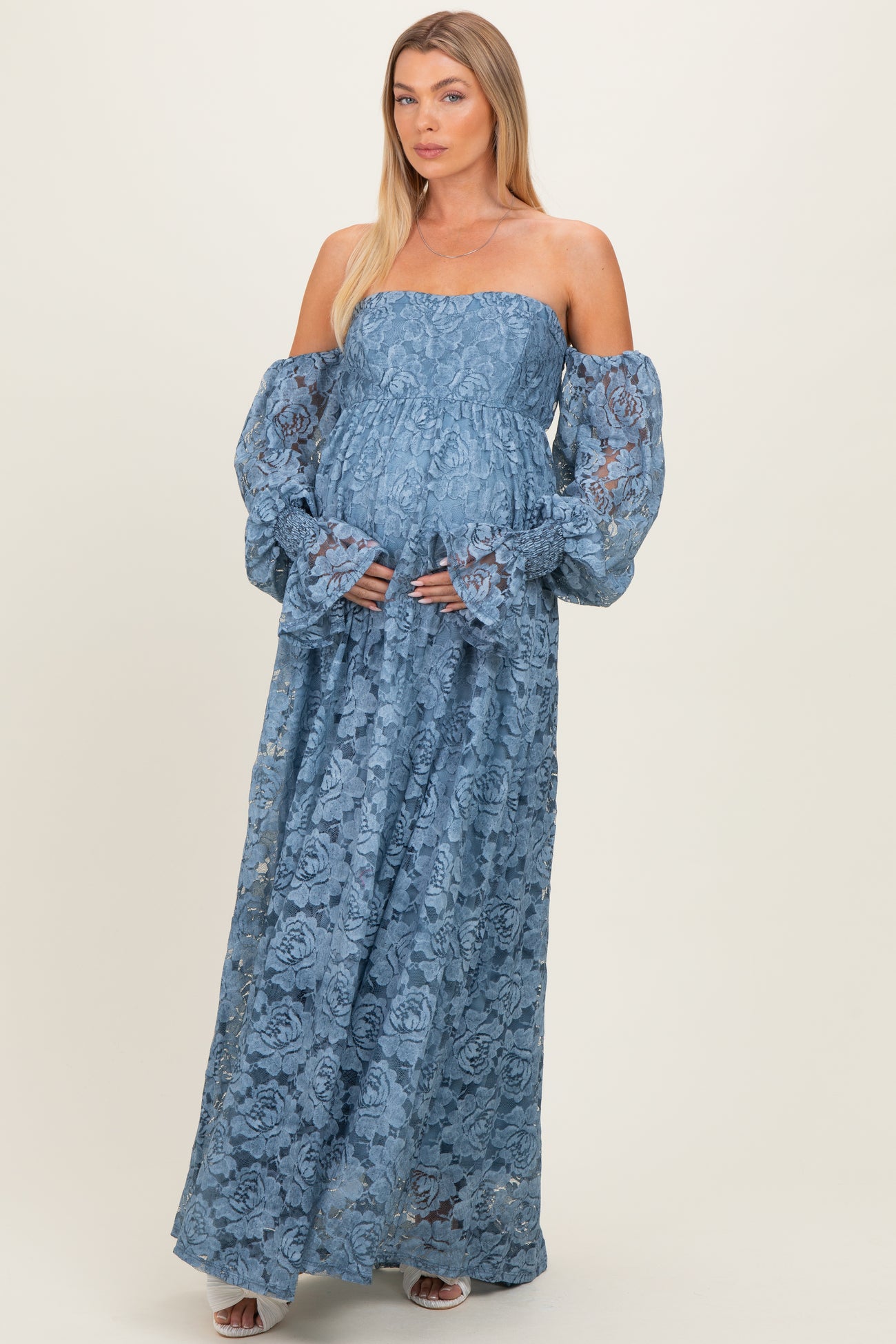 woman wearing a light blue off-the-shoulder lace maxi dress with bell sleeves and holding her baby bump