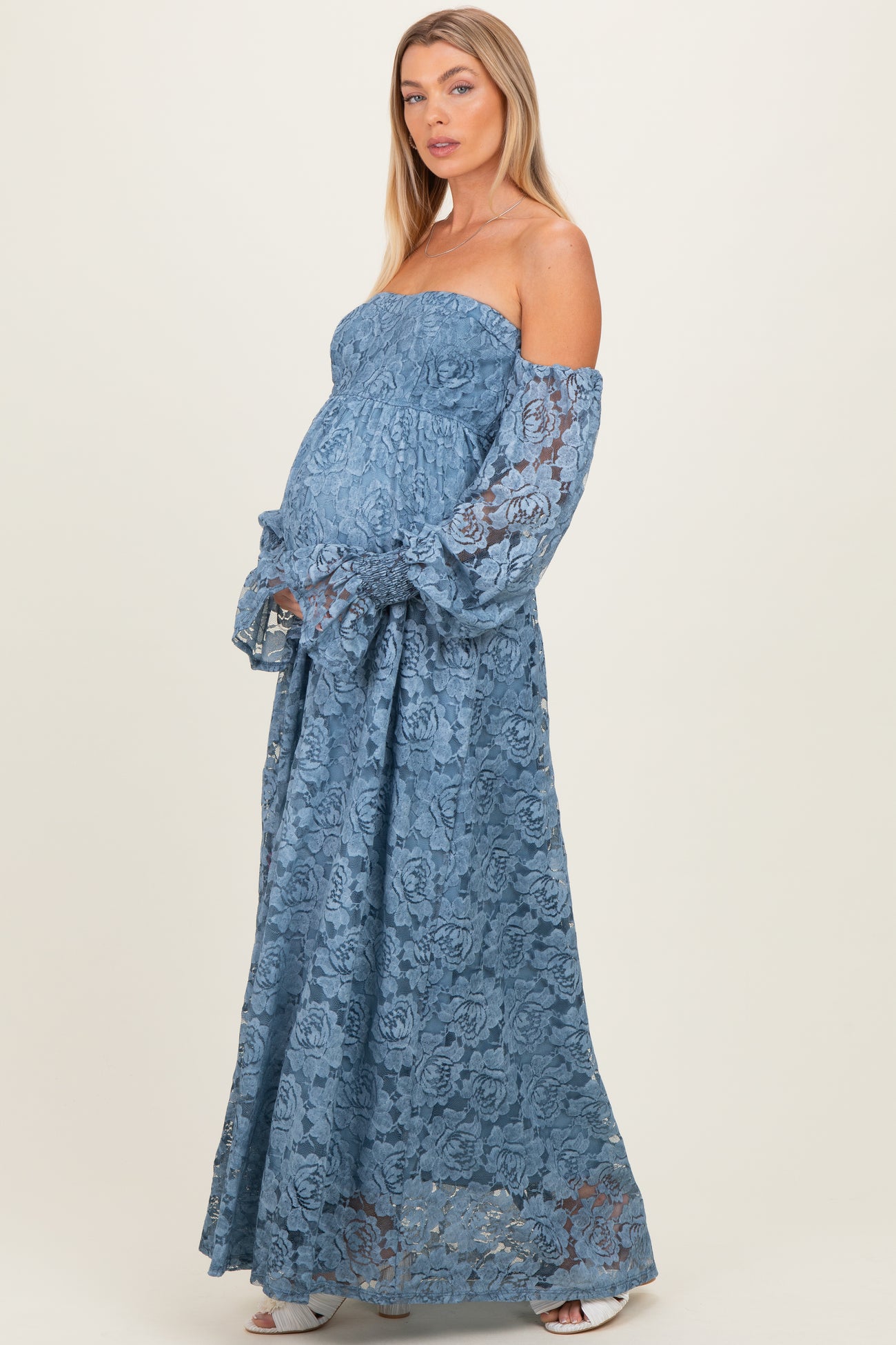 woman wearing a blue lace maternity gown with off-the-shoulder sleeves and a visible baby bump
