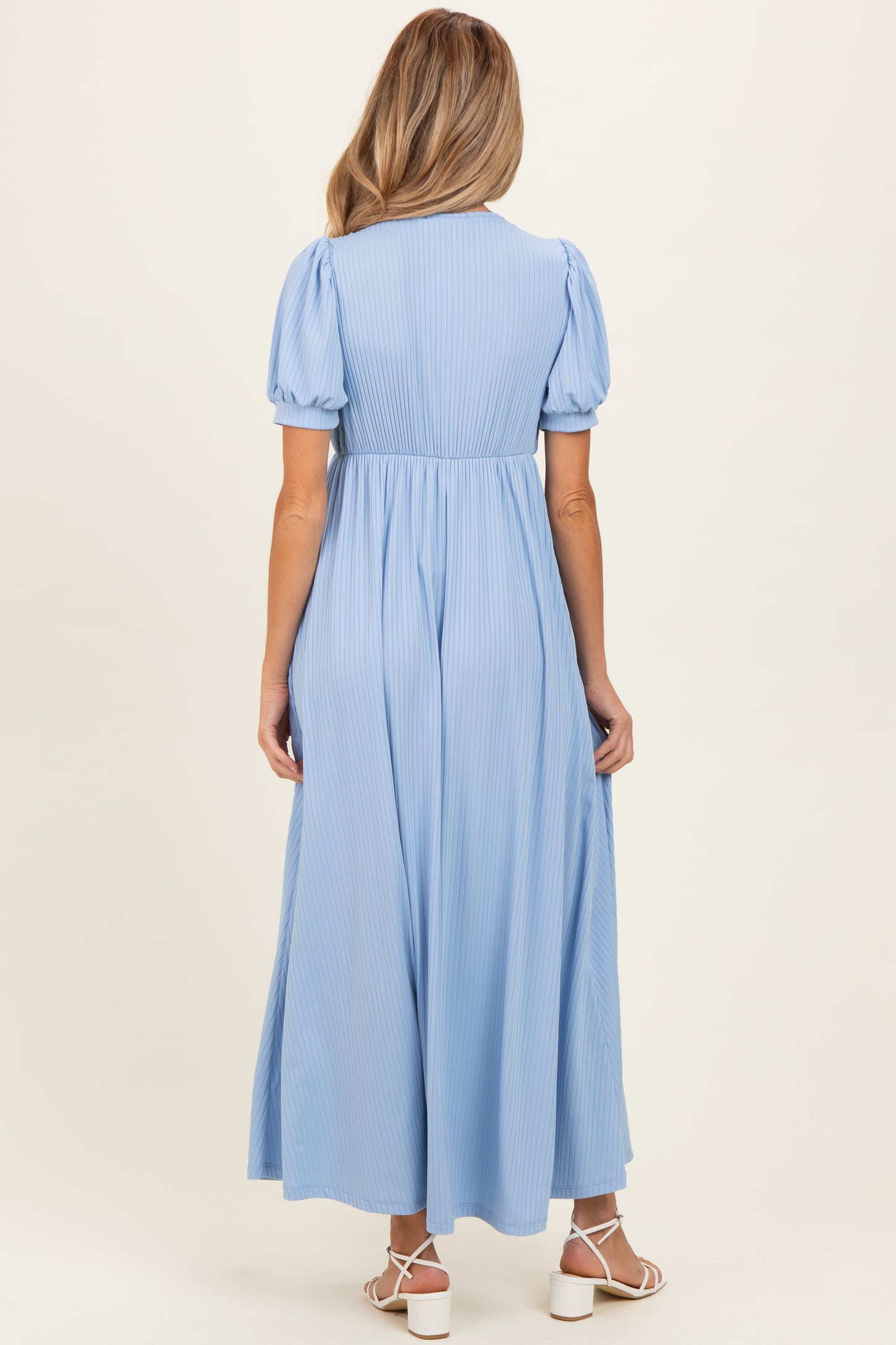 woman wearing a light blue maternity dress with short puff sleeves and a flowing maxi length, showing her baby bump