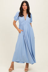 woman wearing a light blue maxi dress with short puff sleeves and a deep V-neck, featuring side pockets and styled with heels