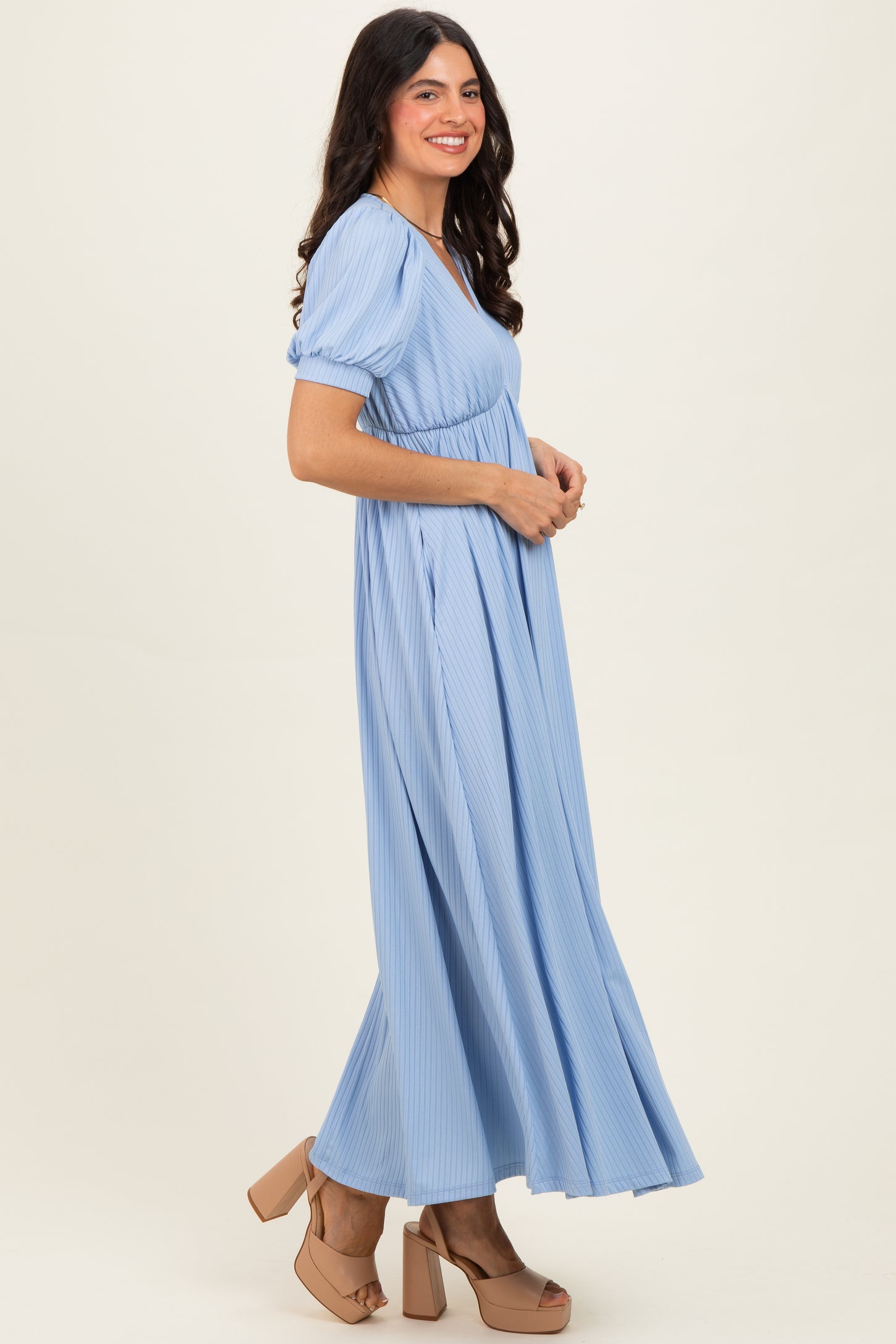 woman wearing a light blue pleated maxi dress with puff sleeves and standing in profile