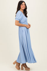 woman wearing a light blue pleated maxi dress with puff sleeves and standing in profile