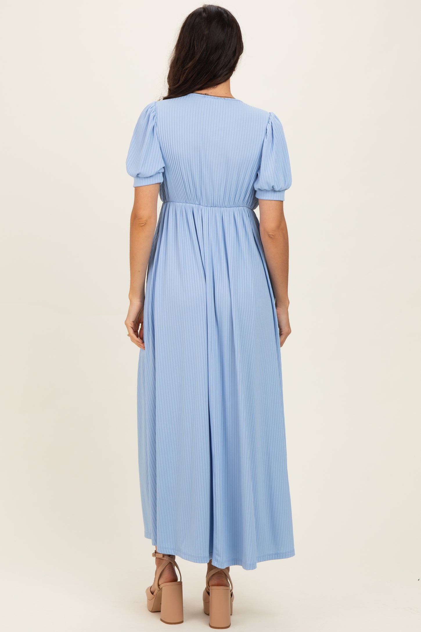 woman wearing a light blue pleated maxi dress with short puff sleeves and a fitted waist from the back