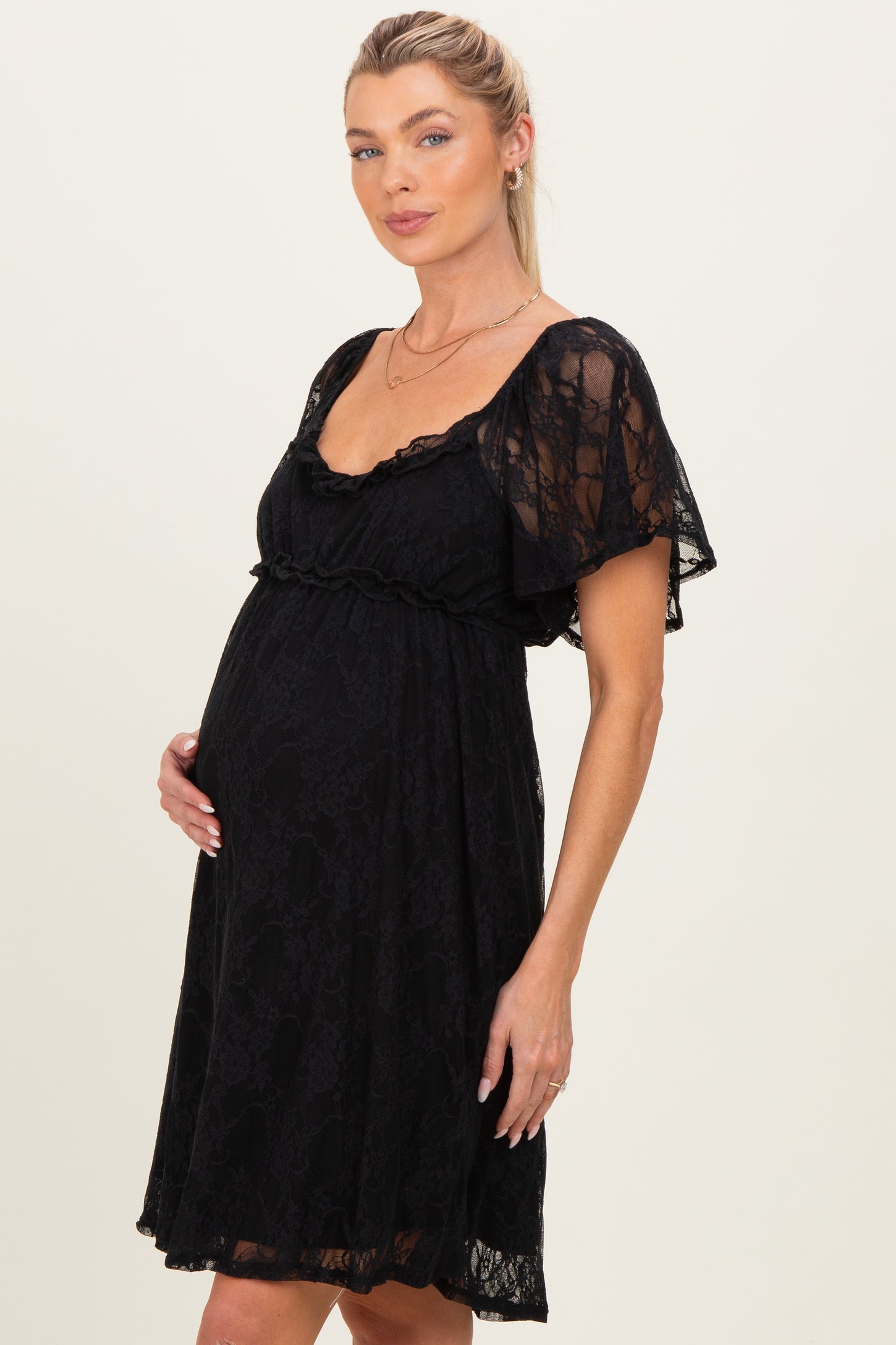 woman wearing a black lace maternity dress with short sleeves and a flowing silhouette, cradling her baby bump