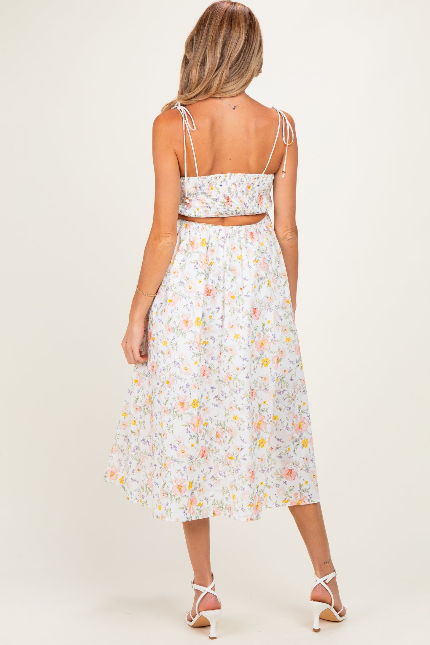 woman wearing a floral maternity two-piece dress with adjustable straps and a flowy skirt, showing her baby bump from the back