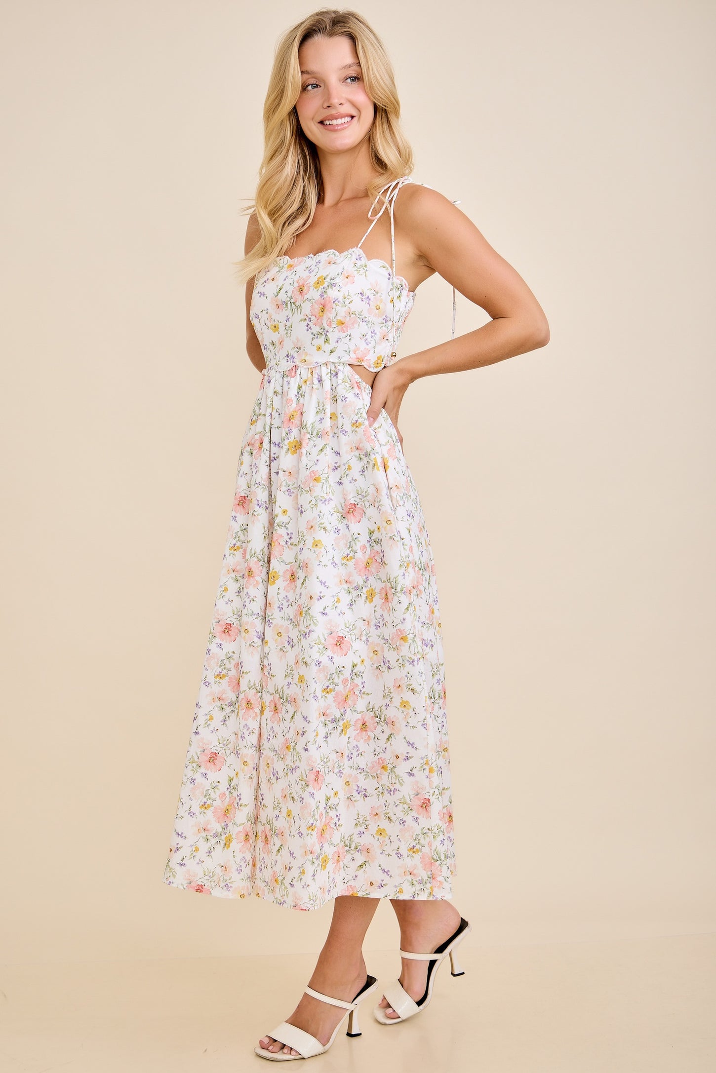 woman wearing a floral midi dress with spaghetti straps and a fitted bodice, standing in a light pose on a neutral background