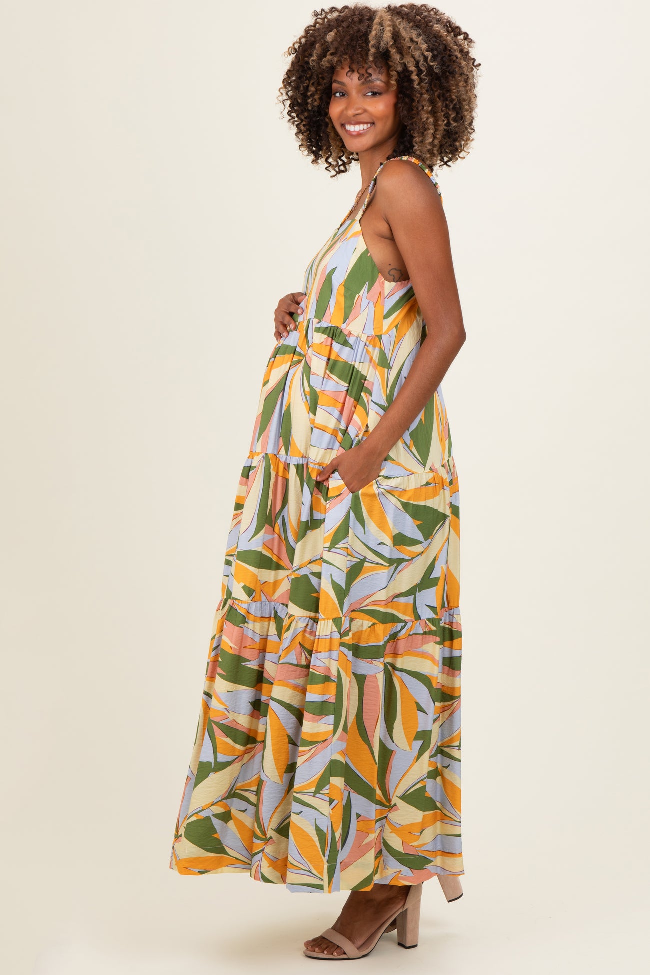 woman wearing a colorful leaf print maternity maxi dress with adjustable straps and pockets, showing her baby bump