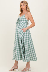 woman wearing a green and white gingham maternity dress with a tie front and pockets, highlighting her baby bump