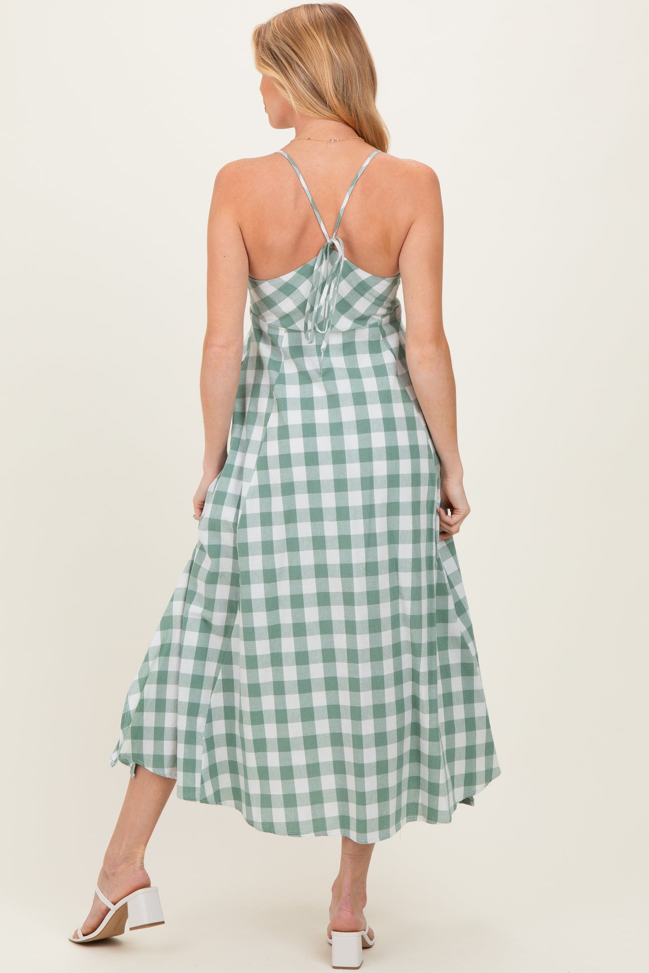 woman wearing a green and white gingham patterned maternity dress with spaghetti straps and a flowy skirt, back view