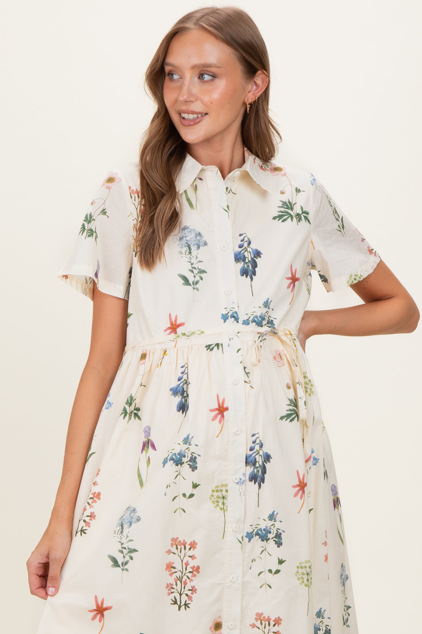 woman wearing a floral button-up maternity dress with short sleeves and a tie waist, showcasing her baby bump
