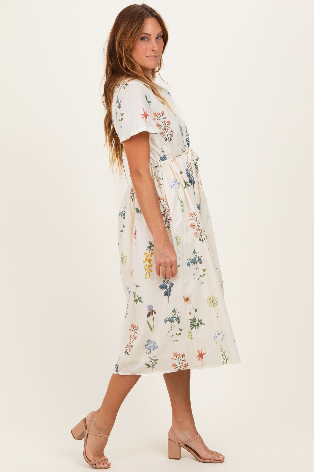 woman wearing a floral print midi dress with short sleeves and a tied waist, posing sideways against a neutral background