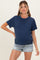 woman wearing a navy blue short sleeve maternity top and denim shorts, posing with one hand on her hip