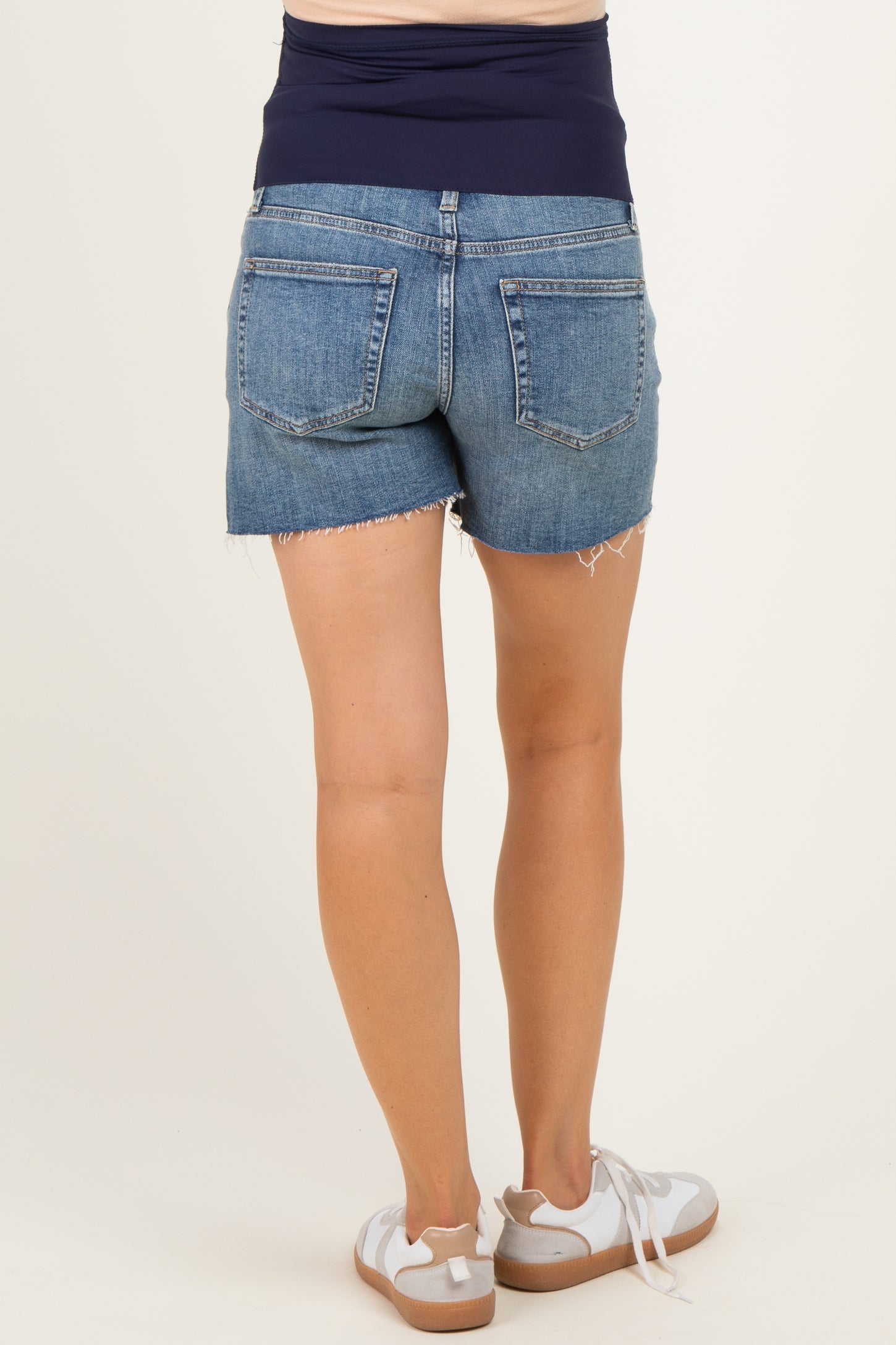 woman wearing dark wash maternity denim shorts with a stretchy waistband and frayed hem, viewed from the back