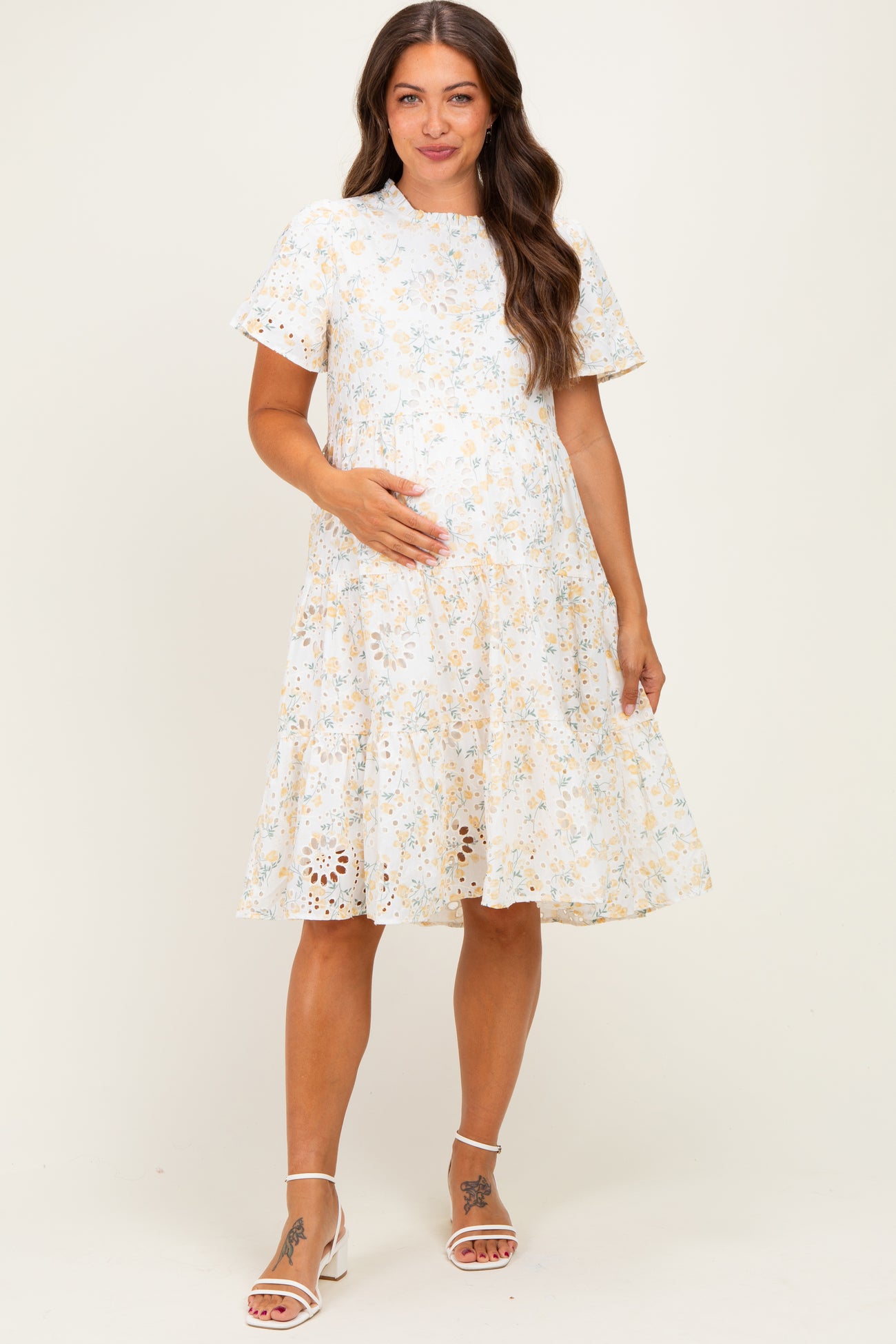 woman wearing a floral print maternity dress with short sleeves and a flared skirt, holding her baby bump