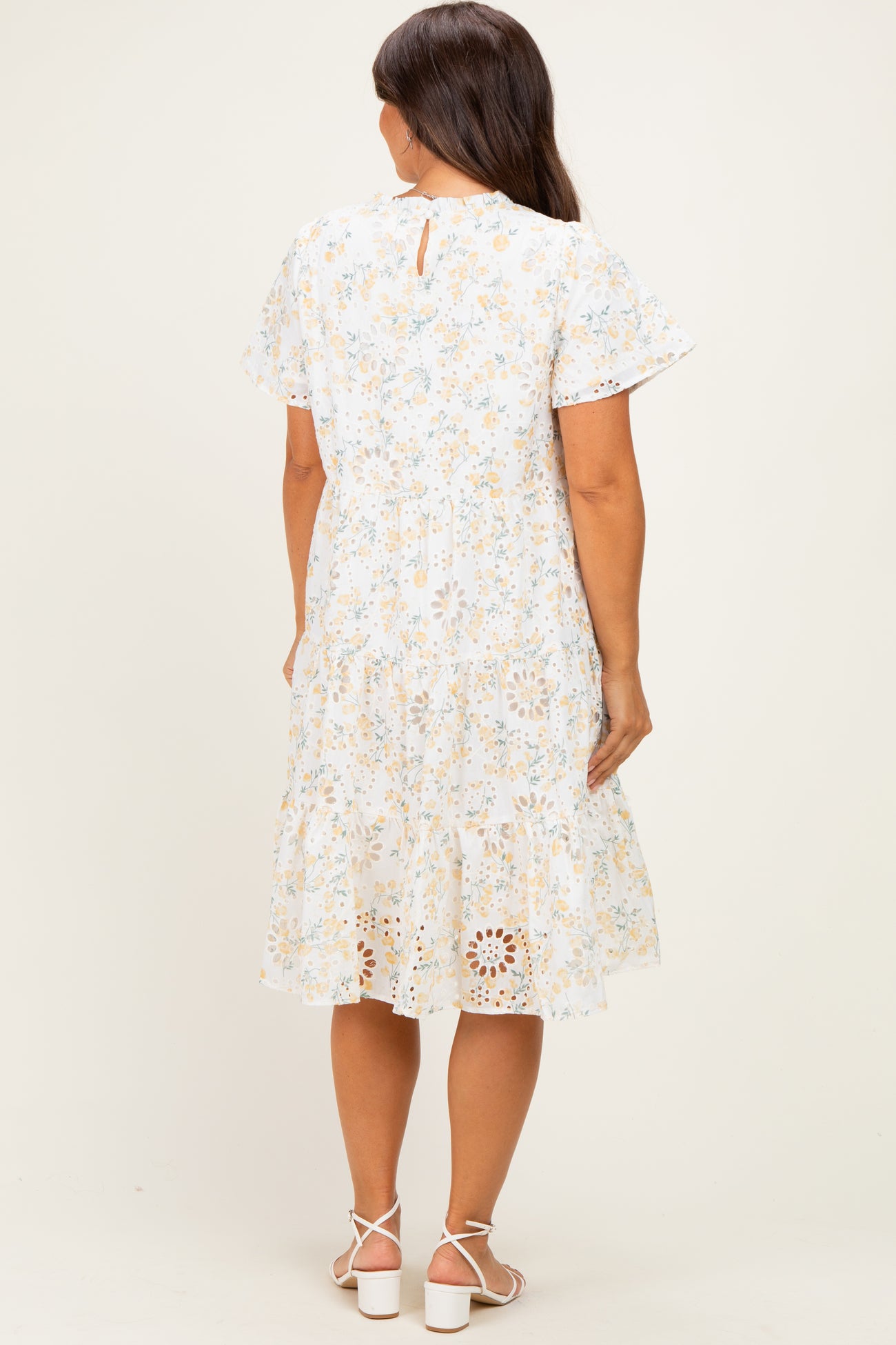 woman wearing a white floral maternity dress with short sleeves and a tiered skirt, showing a baby bump