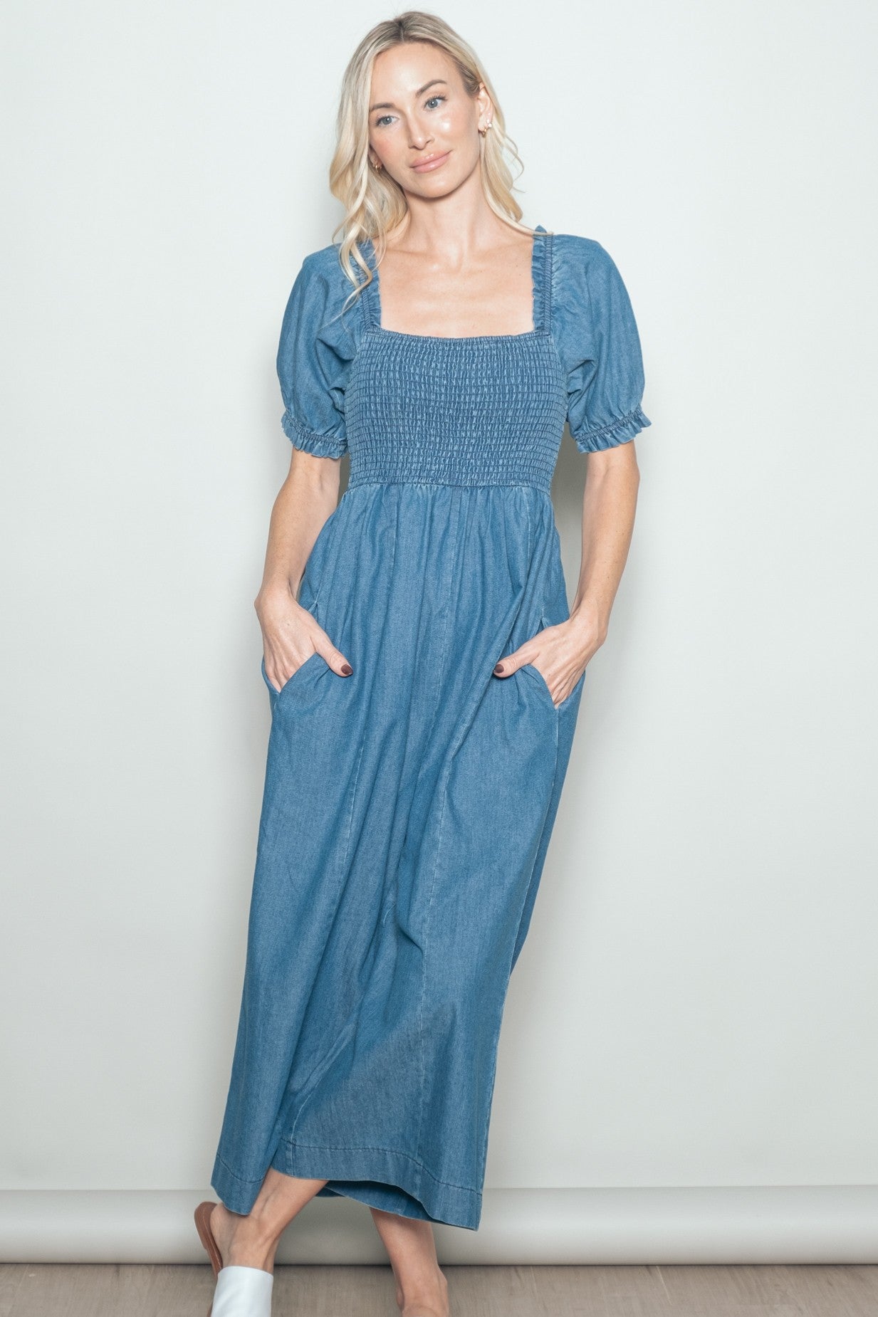 woman wearing a blue denim maxi dress with short puff sleeves and a smocked bodice, hands in pockets