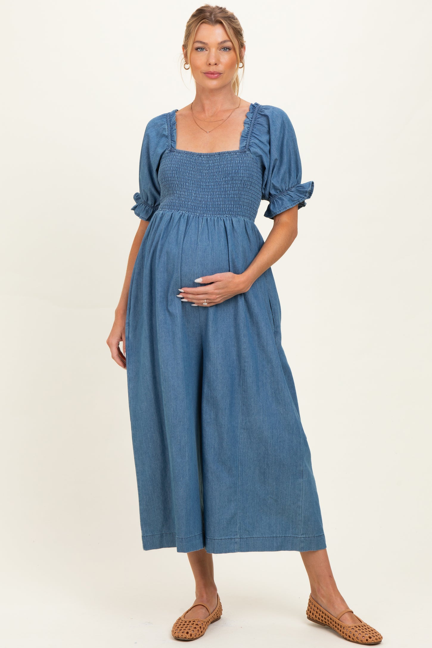 woman wearing a blue denim maternity dress with a smocked bodice and puff sleeves, holding her baby bump