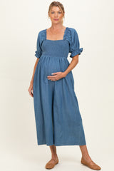 woman wearing a blue denim maternity dress with a smocked bodice and puff sleeves, holding her baby bump