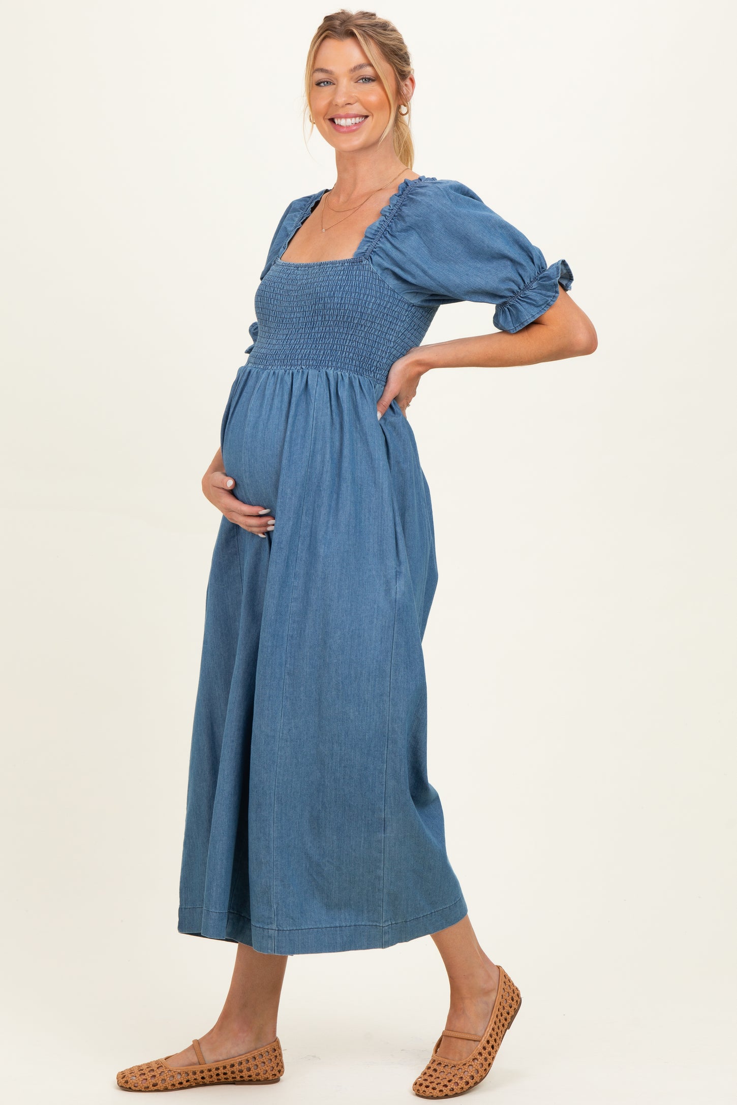 woman wearing a blue denim maternity dress with puff sleeves and a fitted bodice, showcasing her baby bump
