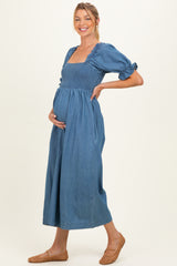 woman wearing a blue denim maternity dress with puff sleeves and a fitted bodice, showcasing her baby bump