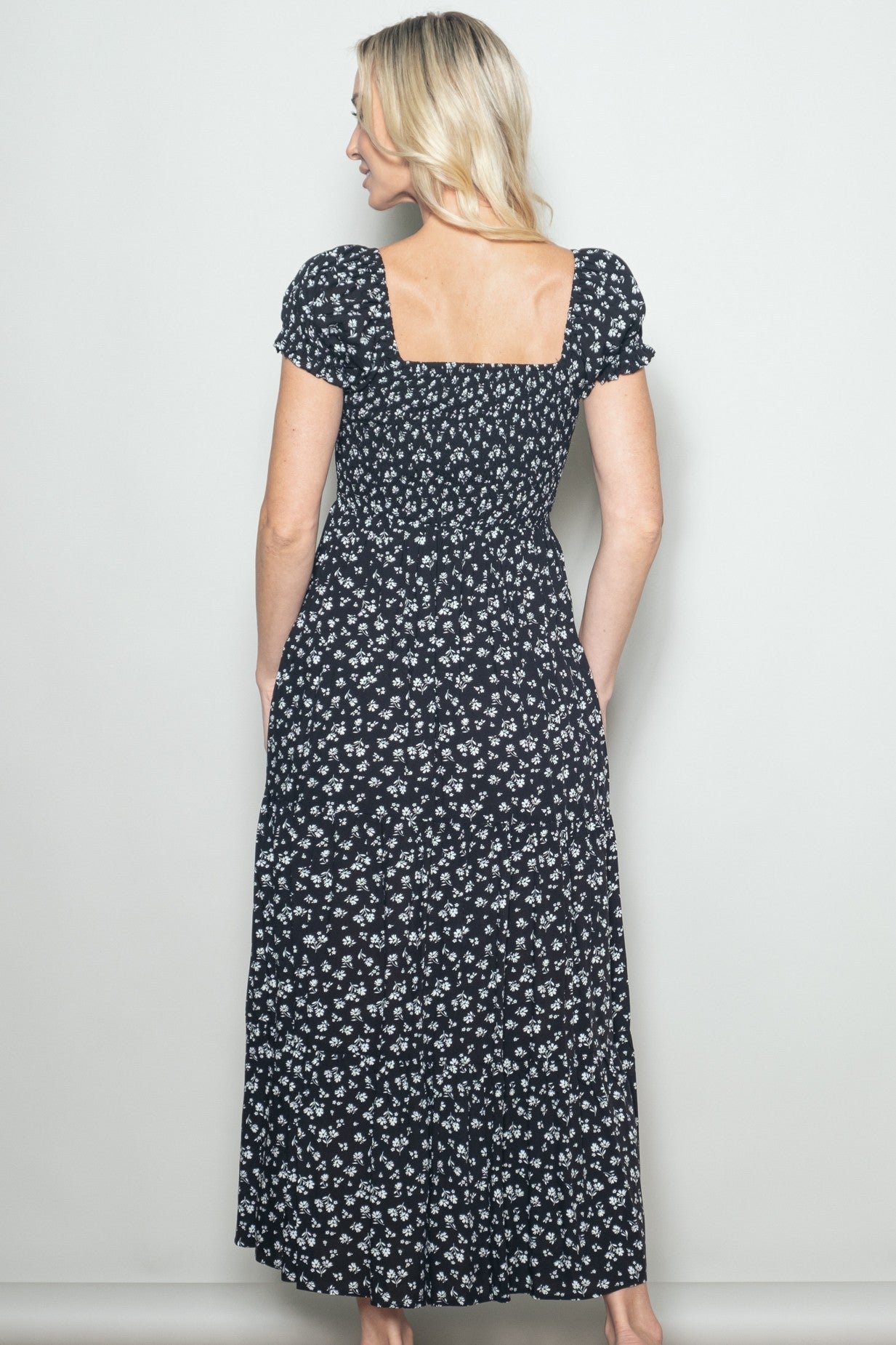 woman wearing a black floral maxi dress with a square neckline and short puff sleeves, showing the back view