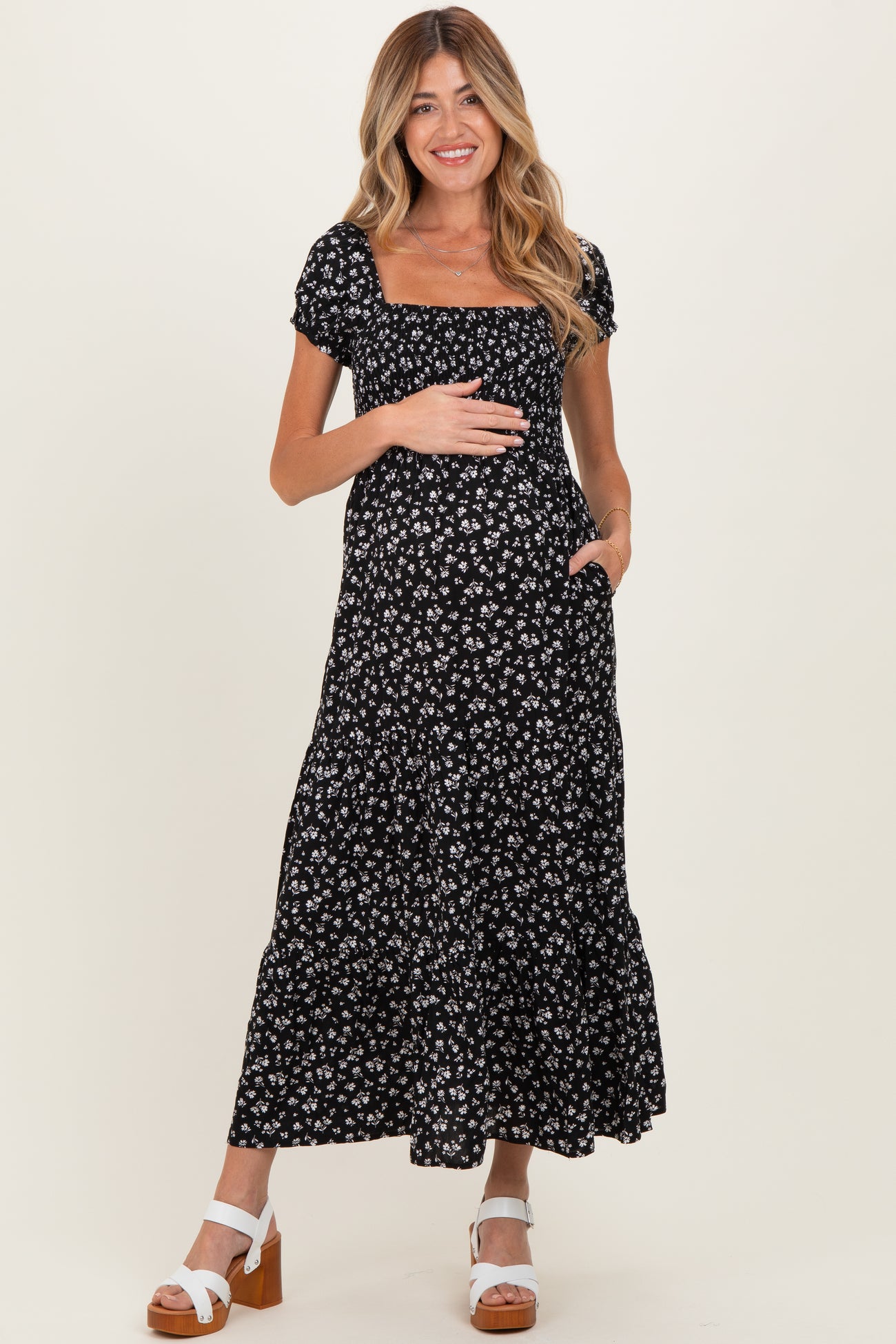woman wearing a black floral maternity maxi dress, holding her baby bump and smiling