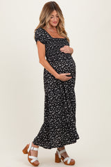 woman wearing a black floral print maternity dress and holding her baby bump