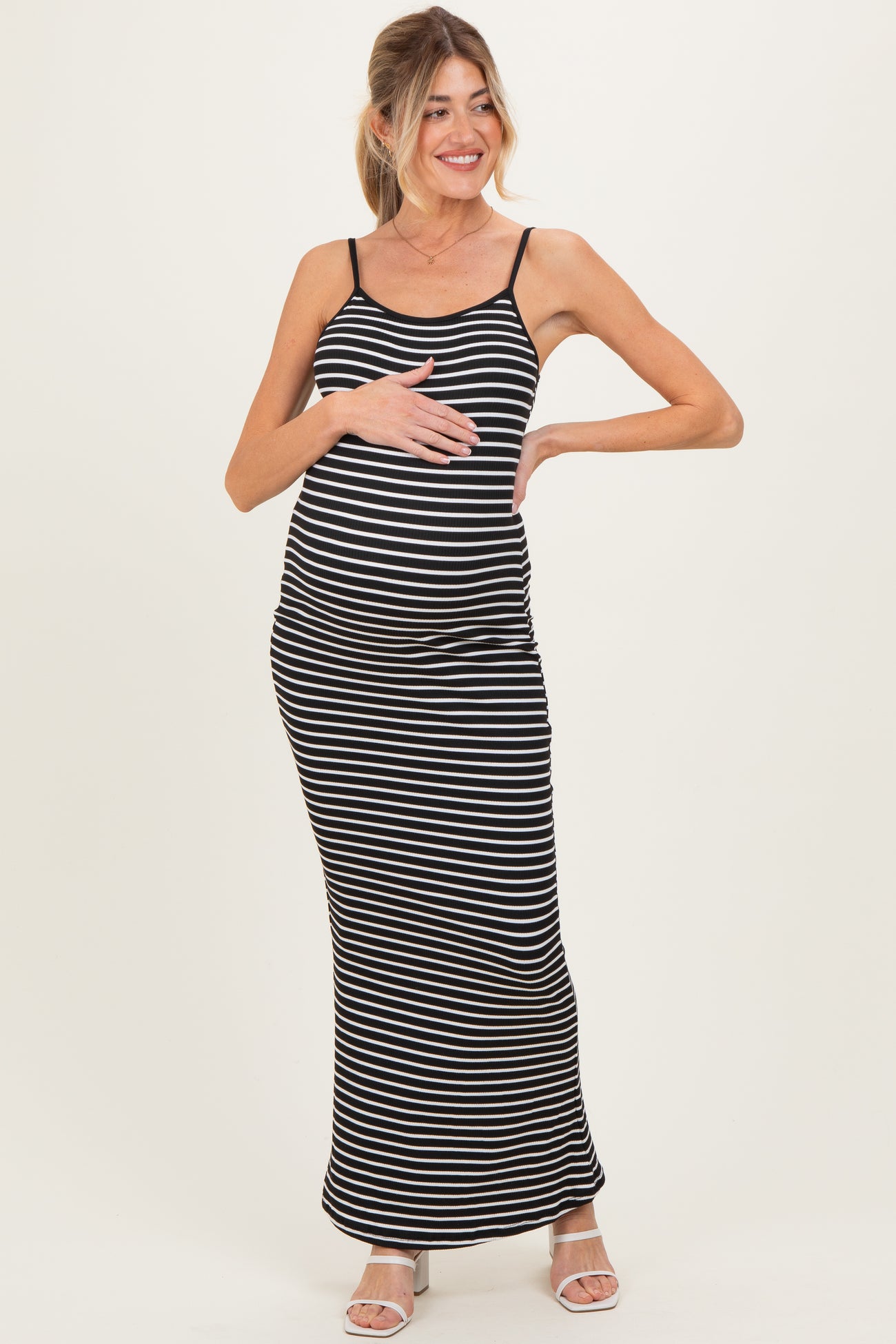 woman wearing a black and white striped maternity maxi dress and gently cradling her baby bump