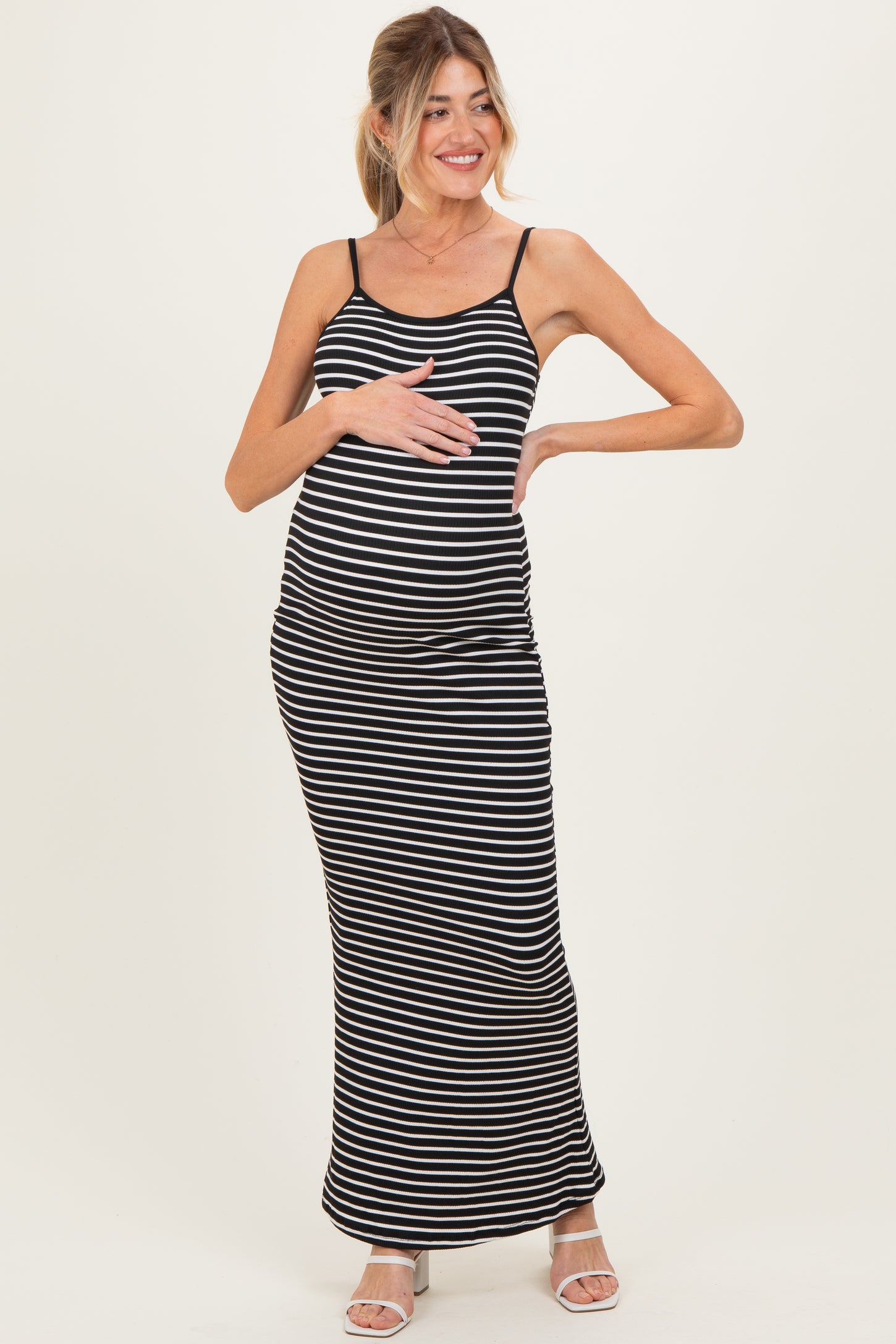 woman wearing a black and white striped maternity maxi dress and gently cradling her baby bump