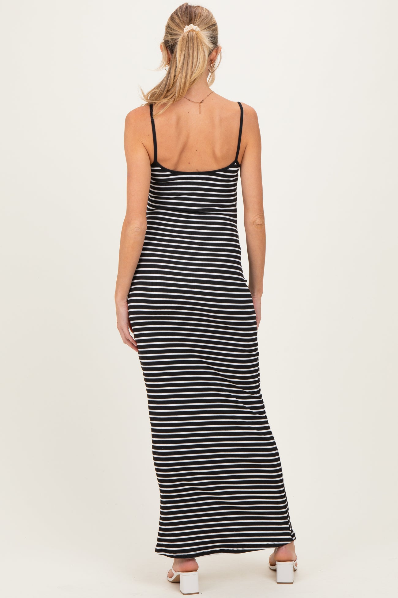woman wearing a black and white striped maternity maxi dress with spaghetti straps, showing her back