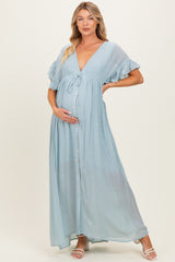 woman wearing a light blue maternity maxi dress with ruffled sleeves and a button-down front, gently holding her baby bump
