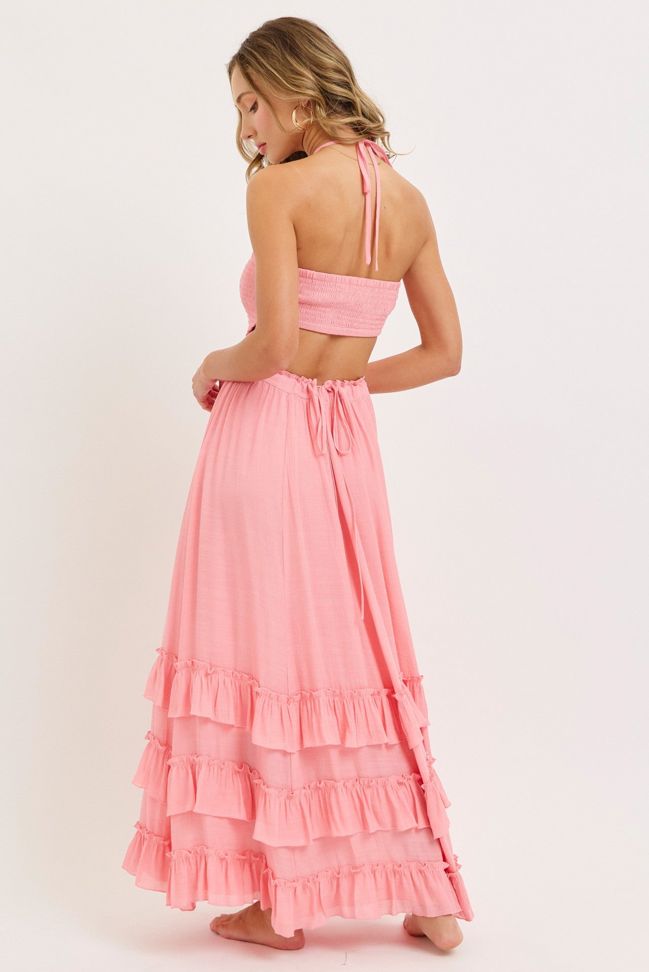 woman wearing a pink halter neck dress with a tiered ruffle hem and open back design