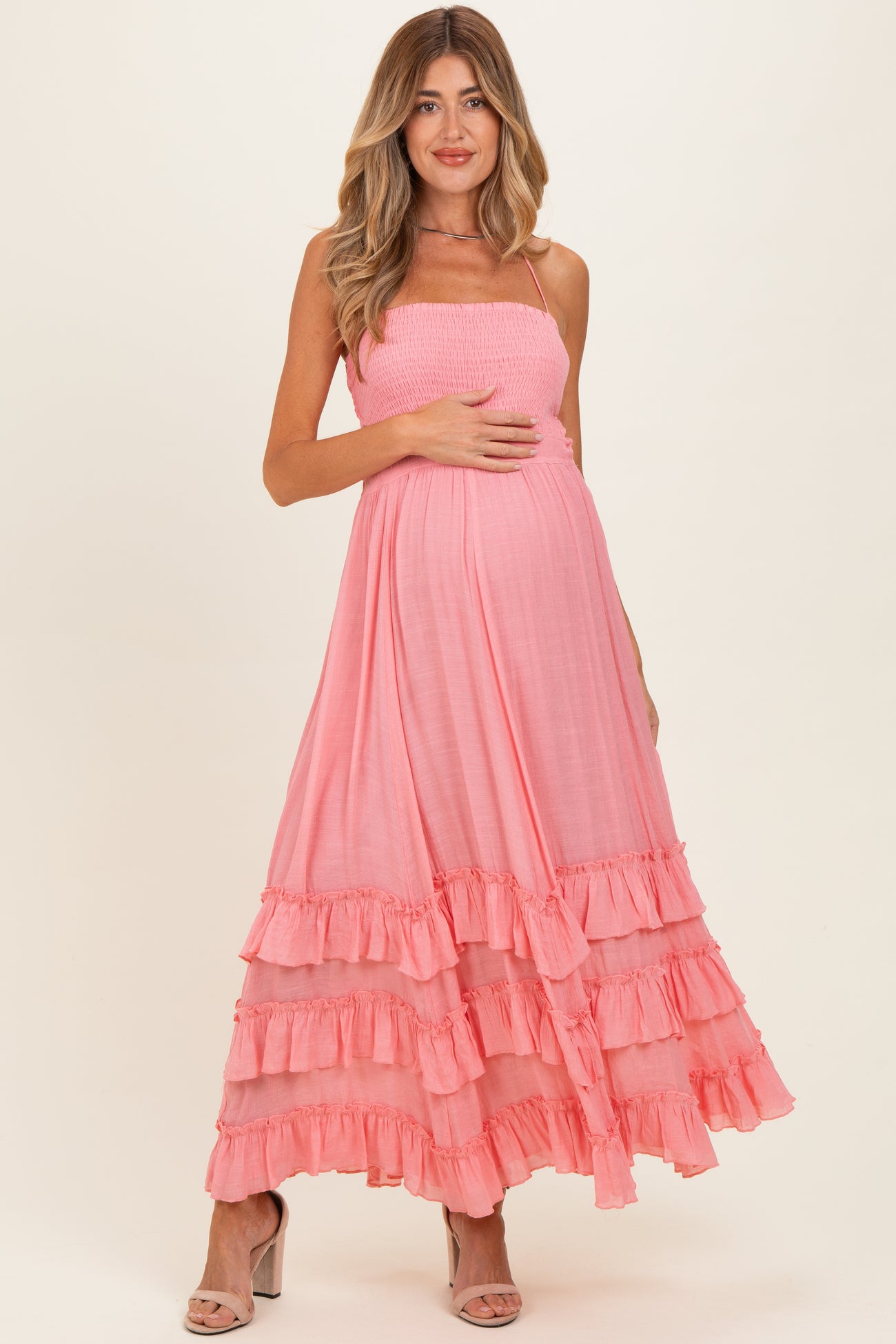 woman wearing a pink maternity maxi dress with ruffles, holding her baby bump