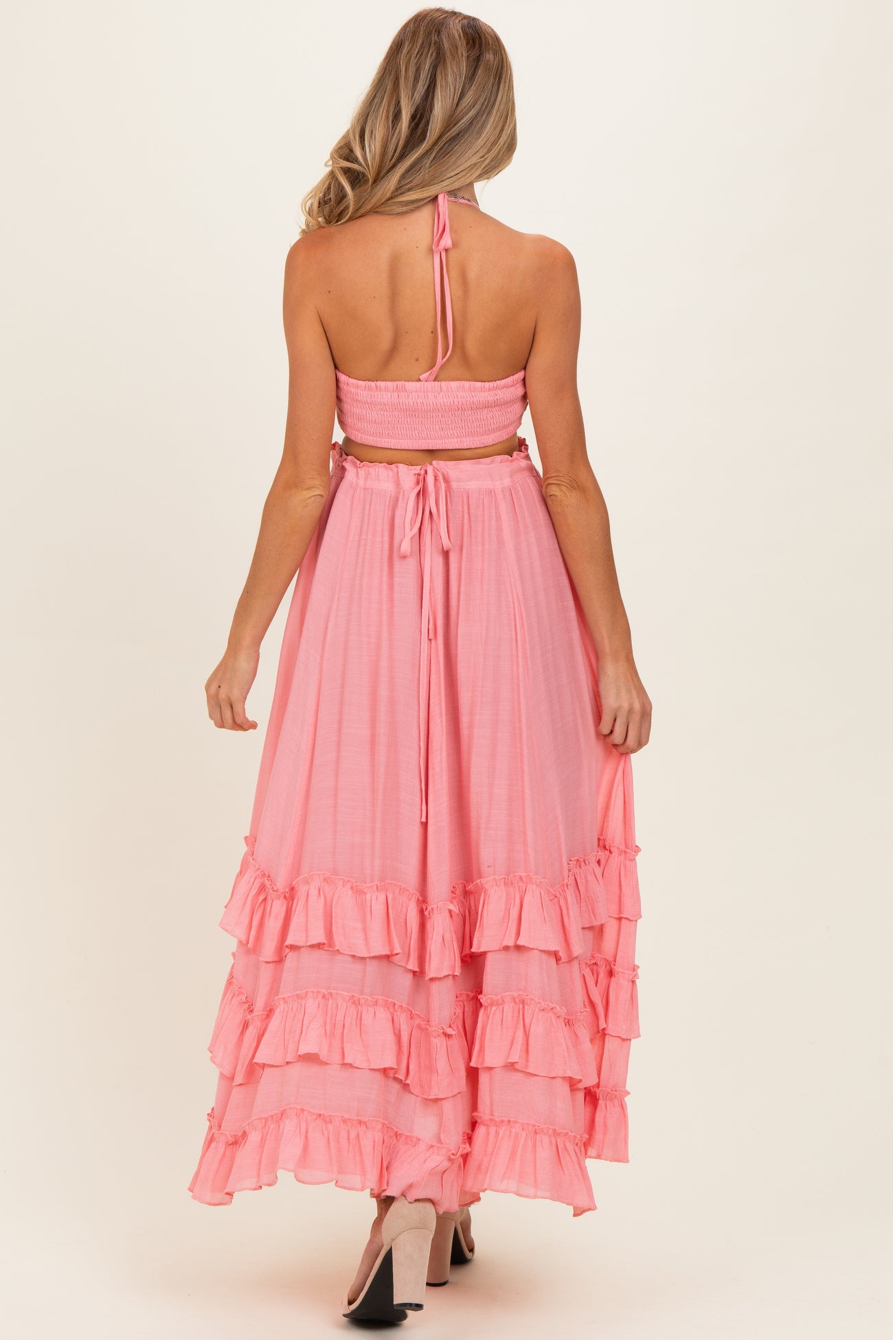 woman wearing a pink maternity maxi dress with ruffled tiers and a tie-back halter neck