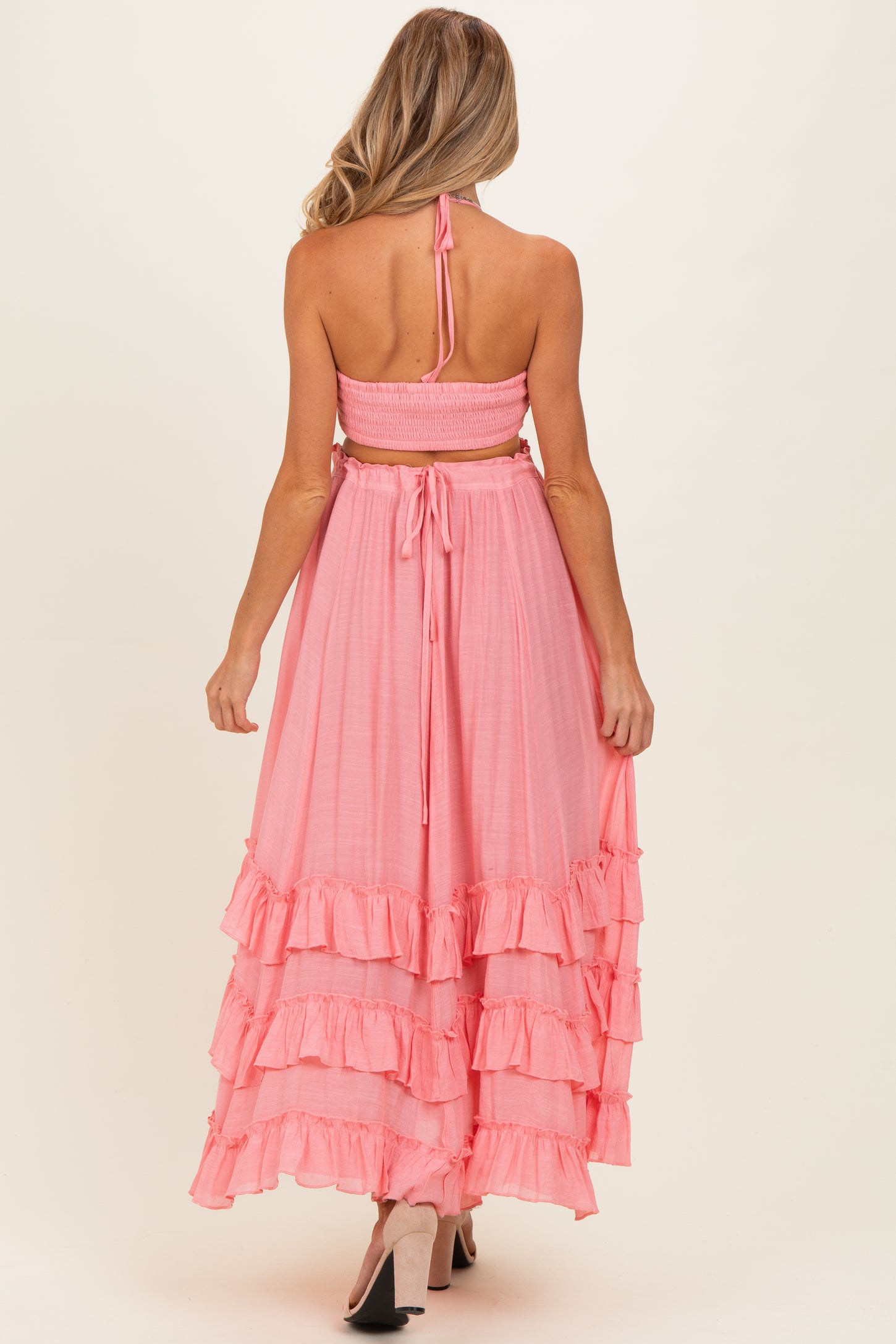 woman wearing a pink maternity maxi dress with ruffled tiers and a tie-back halter neck