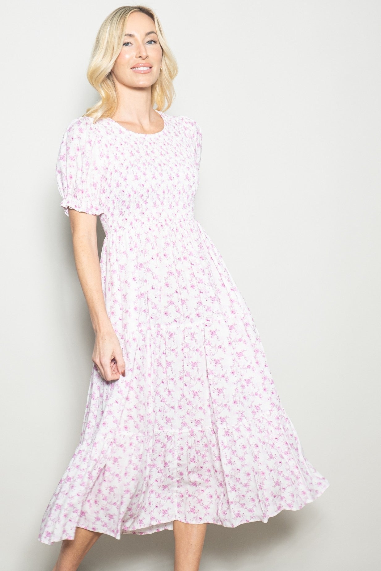 woman wearing a pink floral midi dress with short puff sleeves and a tiered skirt, smiling at the camera