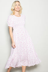 woman wearing a pink floral midi dress with short puff sleeves and a tiered skirt, smiling at the camera