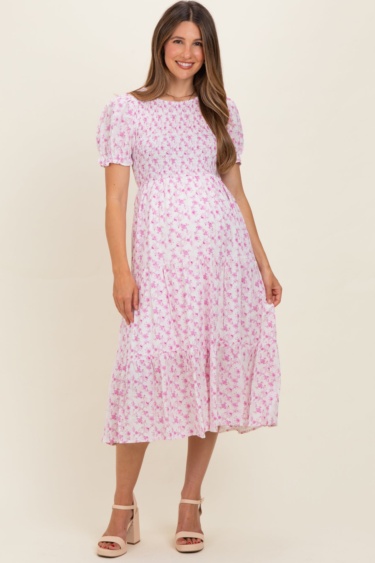 woman wearing a pink floral maternity dress with puff sleeves and a tiered skirt, showcasing a baby bump
