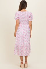 woman wearing a pink floral maternity dress with puff sleeves and a smocked bodice, showing a baby bump