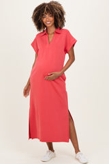 woman wearing a coral maternity dress with short sleeves and side slits, gently holding her baby bump