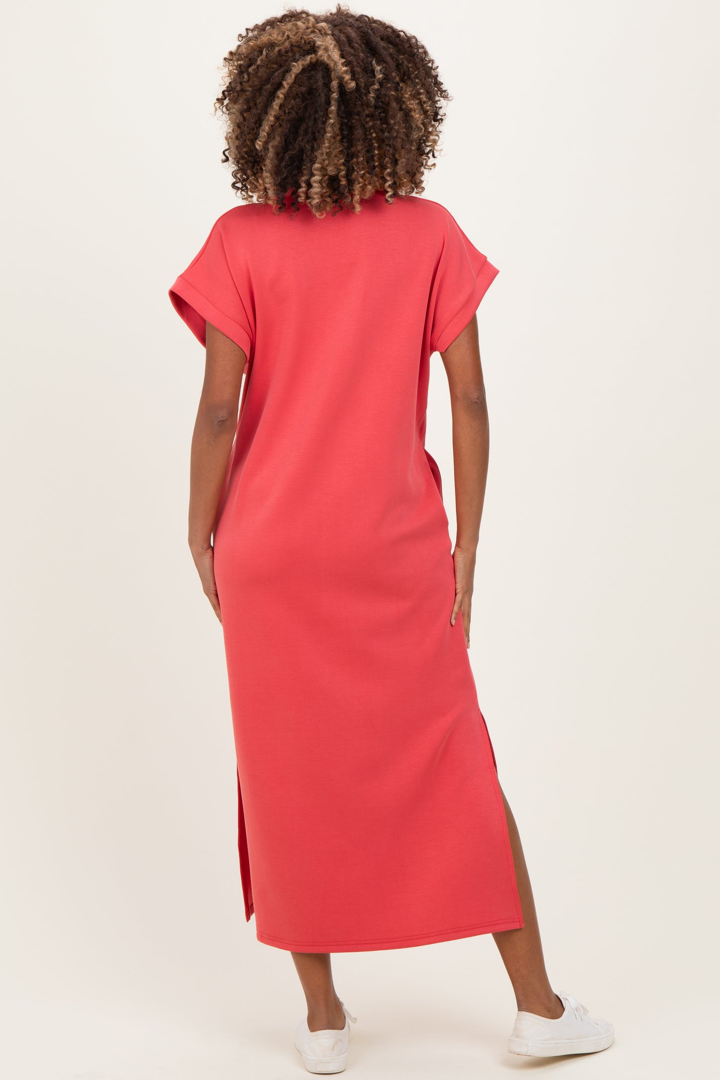 woman wearing a coral maternity maxi dress with short sleeves and side slits, showing her back and hair texture