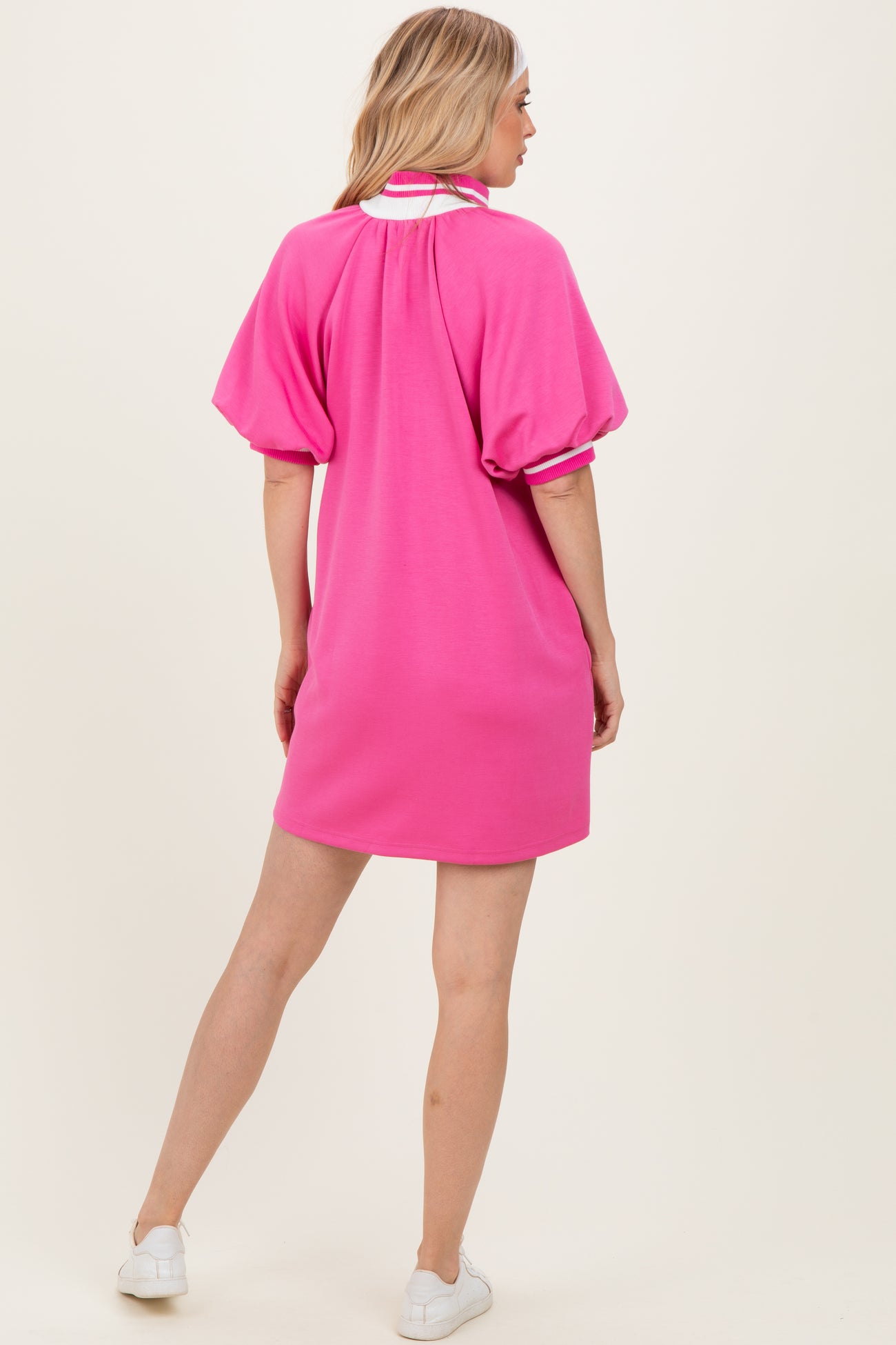 woman wearing a bright pink oversized short sleeve dress, styled with a sporty collar and back pleat details