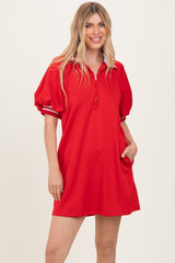 woman wearing a red short sleeve polo dress with puff sleeves and a zipper detail at the neck, standing with one hand in her pocket