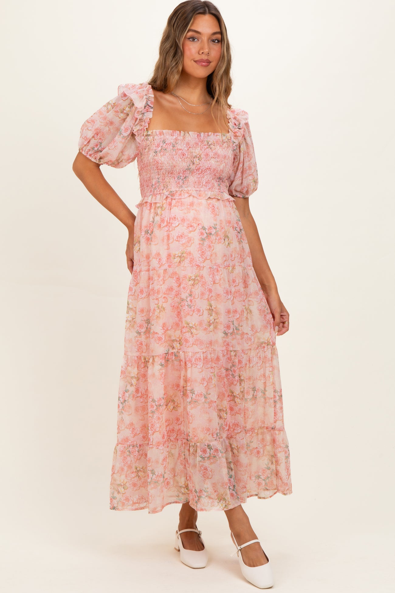 woman wearing a pink floral maternity maxi dress with puff sleeves and smocked bodice, smiling at the camera