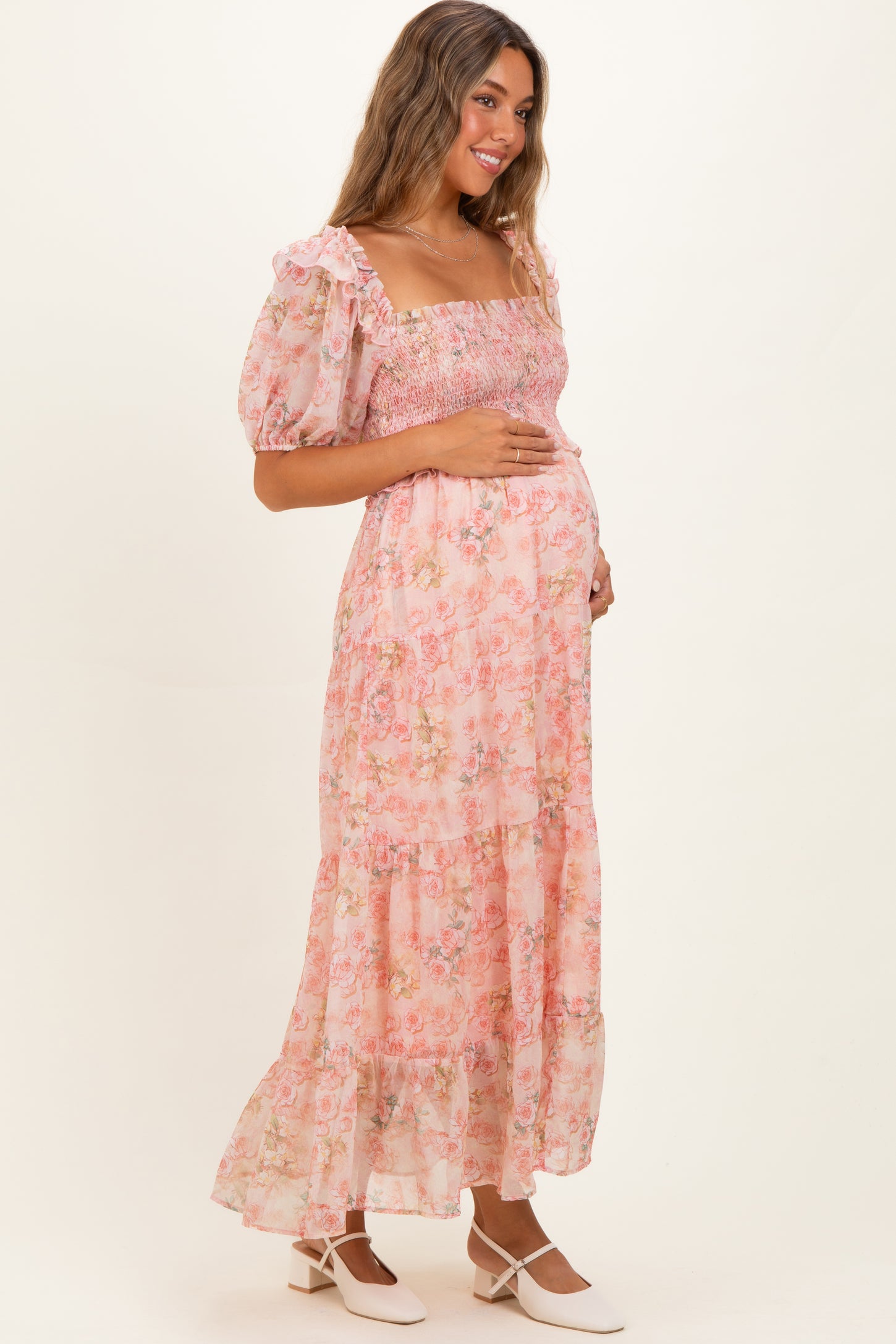 woman wearing a pink floral maternity maxi dress with puff sleeves and holding her baby bump