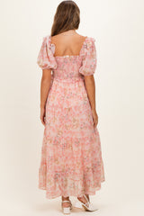 woman wearing a pink floral maternity maxi dress with puff sleeves and a smocked bodice, showing a baby bump from the back