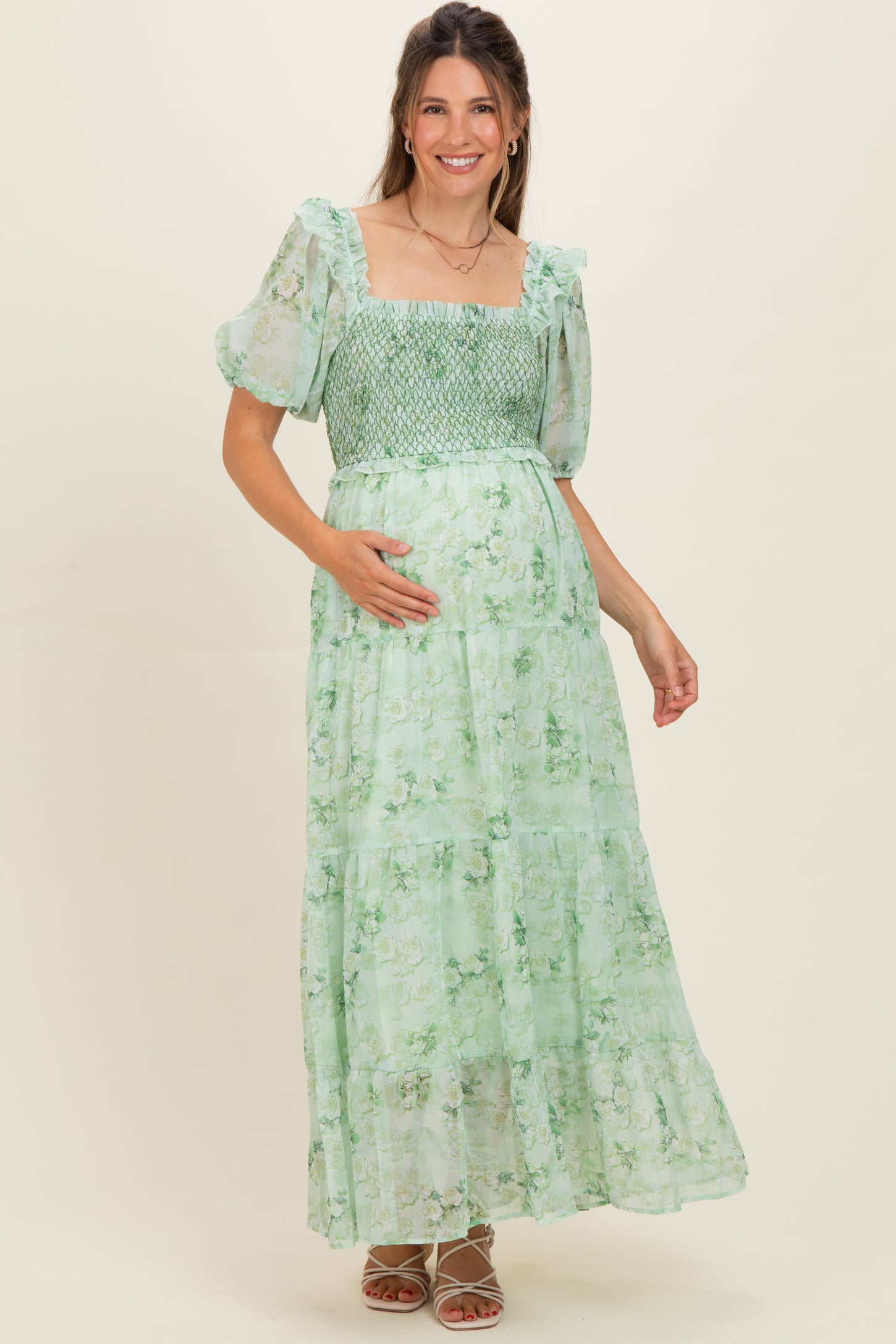 woman wearing a green floral maternity maxi dress with puff sleeves and a smocked bodice, cradling her baby bump