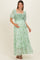woman wearing a green floral maternity maxi dress with puff sleeves and a smocked bodice, cradling her baby bump