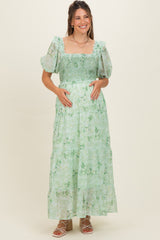 woman wearing a mint green floral maternity maxi dress with puff sleeves and a smocked bodice, holding her baby bump